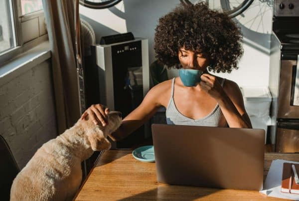 Woman working on laptop with dog in cozy home kitchen.